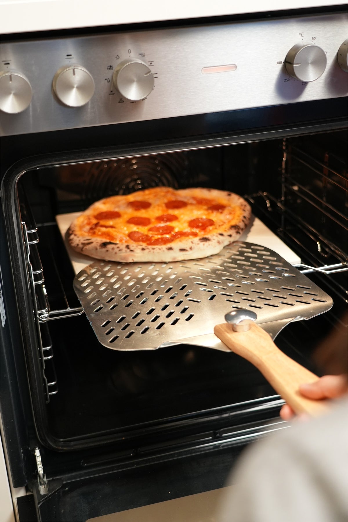 Pizza auf dem Pizzaschieber vor dem geöffneten Backofen