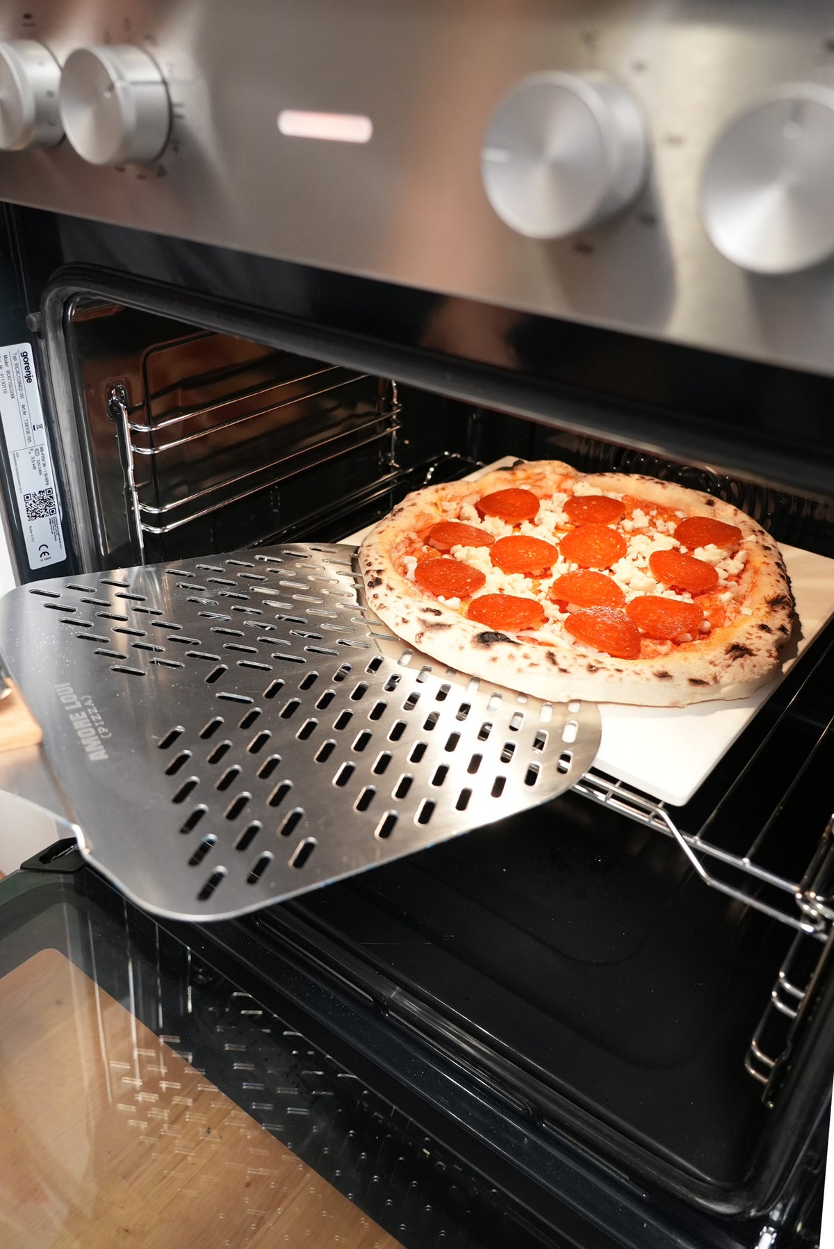 Pizza wird mit dem Pizzaschieber vom Pizzastein genommen