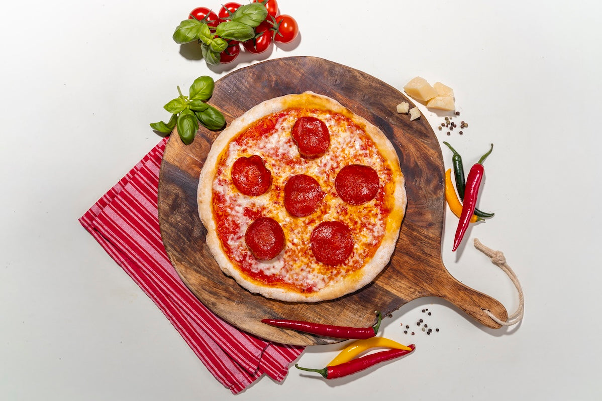 Pizza Diavola glutenfrei auf einem Holzbrett mit Zutaten daneben