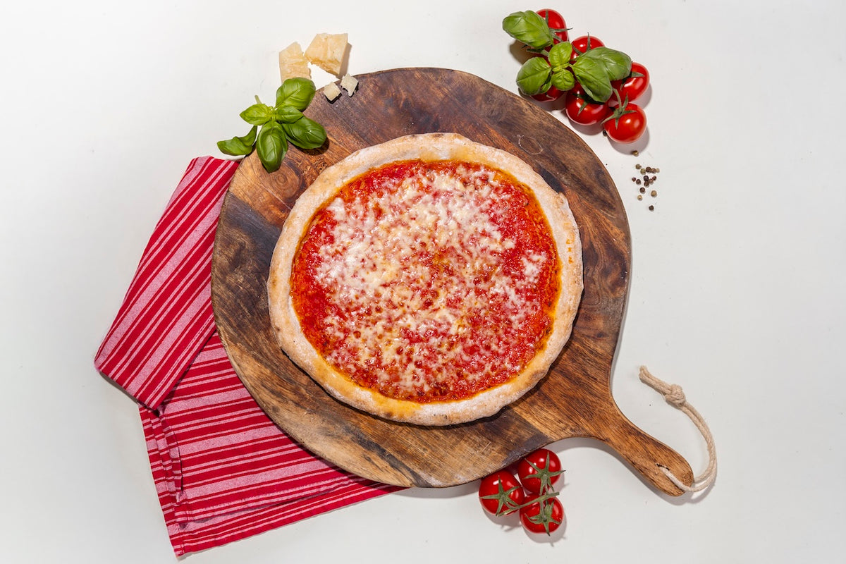 Pizza Margherita glutenfrei auf einem Holzbrett mit Zutaten daneben