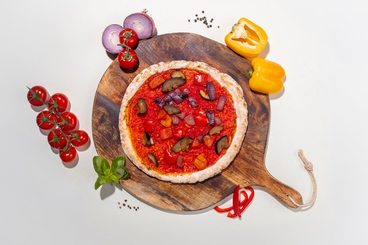 Pizza Mediterran glutenfrei auf einem Holzbrett mit Zutaten daneben