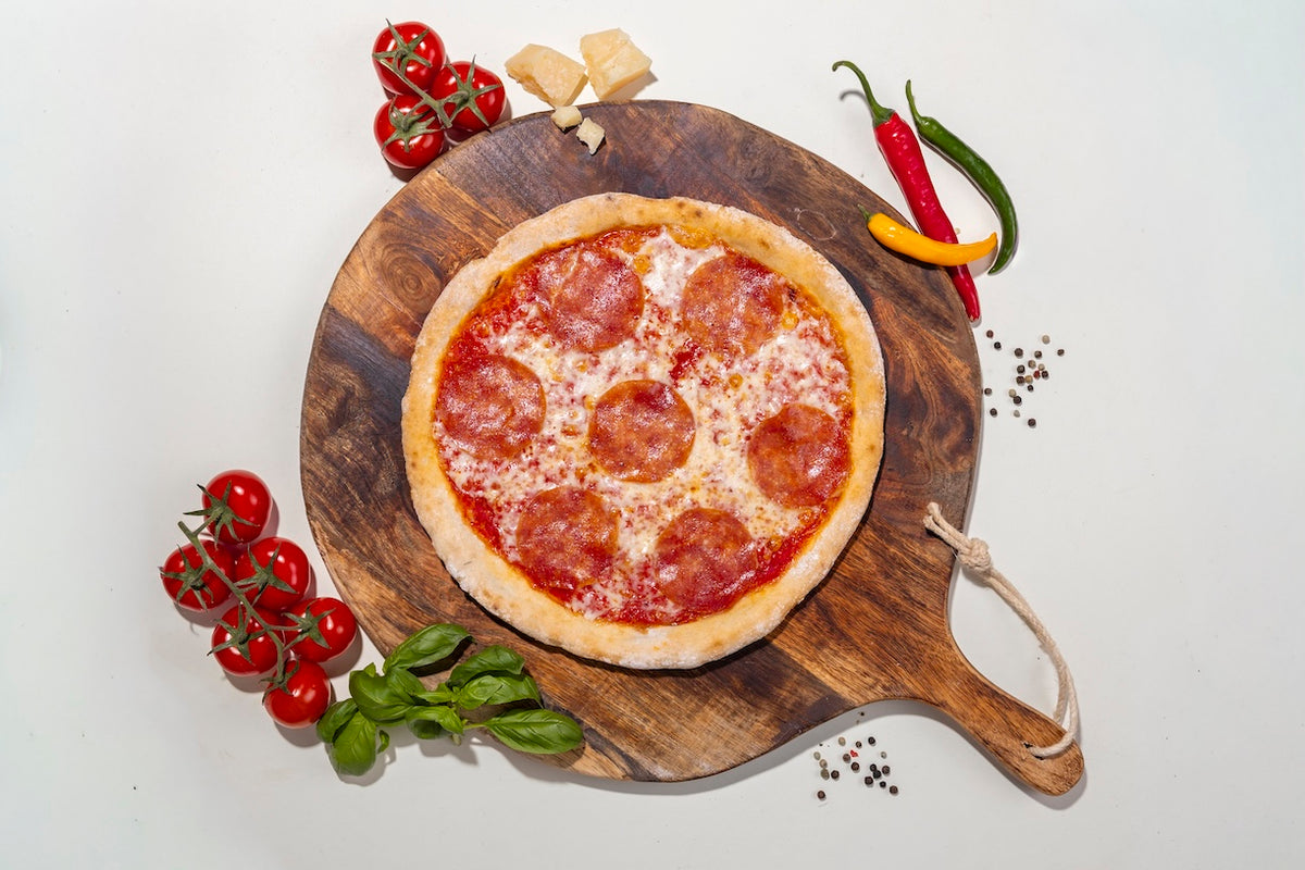 Pizza Salami glutenfrei auf einem Holzbrett mit Zutaten daneben