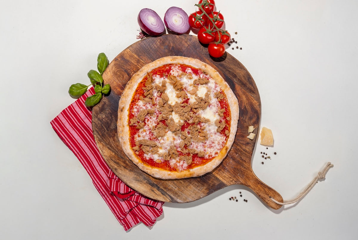 Pizza Tuna glutenfrei auf einem Holzbrett mit Zutaten daneben