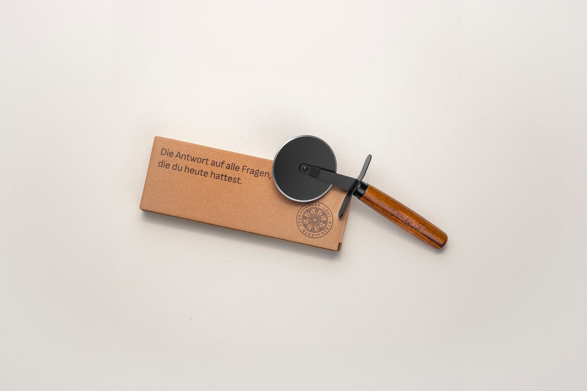 Pizzaschneider mit Holzgriff neben seiner Verpackung, von oben