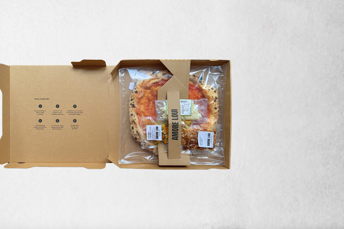 Geöffneter AMORE LOUI Karton mit Pizzaboden und separat verpackten Zutaten